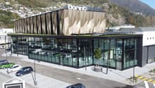 modern building with glass facade, large parking lot, several parked cars, mountains in the background