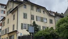 3 story building, beige exterior, multiple windows, green shutters, street light, fence, plants