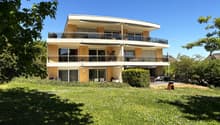 2 story house, yellow exterior, multiple balconies, large windows, surrounded by greenery
