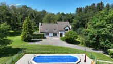 House with brown roof, white walls, 4 windows, driveway, swimming pool, green lawn, hedges, trees