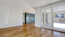 Empty living room with white walls, wooden floor, glass sliding doors leading to a balcony