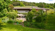 modern house with brown roof, surrounded by trees and garden, vineyard in the background