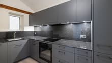 Modern kitchen with grey cabinets, granite countertops, built-in oven, induction cooktop, and modern fixtures.