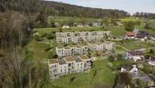 Group of residential buildings with rooftops and terraces, in a valley with trees and meadows