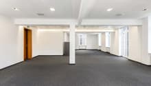 An empty office space with white walls, gray carpet, and a wooden door on the left side.