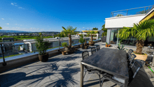 Stone floor, round table, chairs, palm trees, distant buildings, mountain range