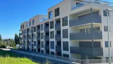 Modern apartment building, multiple floors, balconies, glass railings, white exterior, green grass, street view