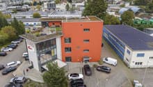 Industrial building with parking space in front, solar panels on the roof, orange facade, large glass windows
