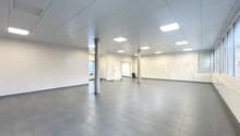 Empty room with grey tiles, white walls, square ceiling lights, and windows with blinds.