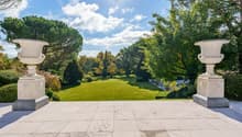 large open green lawn with trees, plants, marble vases, bright blue sky, sunny