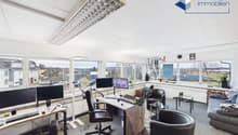 Office with large windows, large desk, 2 computer monitors, black office chairs, couch, and modern decor