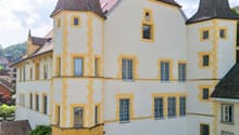 Large white building with yellow trim, two towers, multiple windows, brown roof, car parked in front