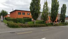 Orange residential building on the street, hedges on the side of the street, trees and bushes around.