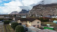 Detached house, brown roof, large yard, garage, located in a hilly, rural area, mountains in the background