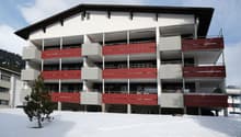 Multi-story building, white exterior, red balconies, covered balconies, located in snowy area, front garden