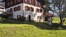 2 story house, brown and white, red shutters, large lawn, tree, mountains in the background