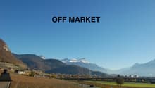 Farmland with rows of grapevines, distant mountains covered in snow, road and a bridge in the distance, a clear sky.
