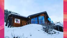 Wooden ski chalet building, big windows, covered by snow, mountain background