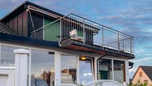 white house, black roof, balcony with metal railing, glass windows, white fence