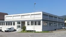 A modern building with many windows, possibly an office or industrial building, cars parked in front, white walls, a van parked in front