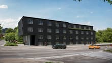 Modern building with multiple windows, flat roof, black exterior, rooftop greenspace, main entrance on the left, a garage visible at the entrance, multiple vehicles in the scene.