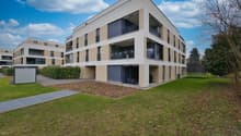 Three story apartment building, balcony on each floor, grey and beige exterior, fenced yard