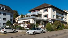 3 story building, white exterior, brown roof, balcony, parking lot, plants, flag