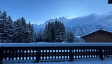 Snow covered balcony railing, snowy landscape, winter mountains, trees, wooden chalet