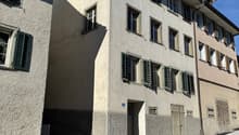 Concrete building with multiple windows and green shutters, street entrance, paved street.