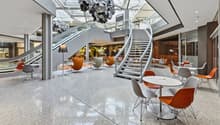 modern interior with white and orange chairs, white tables, large staircase, escalator, glass ceiling