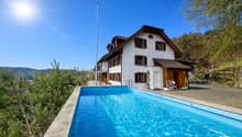 Detached house, white exterior, brown roof, large swimming pool, trees, mountains in the background
