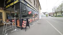 A restaurant with glass walls, a menu board, and outdoor seating.