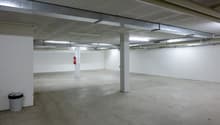empty parking place, white walls, gray floor, ceiling with metal frames, fire extinguisher, white ceiling with fluorescent lamps
