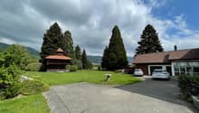 wide lawn, parked cars, detached house in the background, small wooden house, trees, mountains