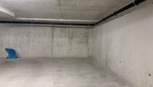 Empty parking space with concrete walls, floor, and ceiling, yellow markings, and a blue plastic bag