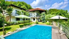 2-story villa, white exterior, red roof, large pool, patio, fence, trees, umbrellas, stairs