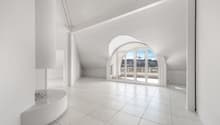 Spacious attic living room with white walls, large arched windows providing a view, and a tiled floor.