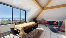 Dining area with a table and chairs, a couch, a TV, a cabinet, a rug, and large windows with a view of the sea