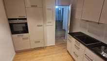 modern kitchen with wooden floor, white cabinets, black countertops, built-in oven, dishwasher, and sink