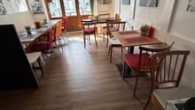 empty restaurant with wooden floor, wooden tables and chairs, white walls, decorative items, and a glass door leading to the outside