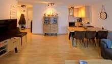 open living area with dining table and couch, wooden floor, large window, TV on stand, kitchen, cabinet, dining table with chairs