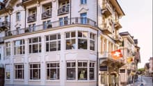 The building is a multistory white building with large windows. It has several floors and a lot of windows. The building looks modern and elegant with no visible exterior balconies. It has a balcony at the top floor. The building also features a triangula