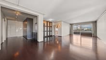 Spacious open-concept living area with hardwood floors, large windows, and a balcony. The room features a modern design with a built-in shelving unit dividing the space. The apartment appears to have a kitchen and other rooms beyond the living area.
