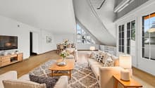 a bright living room with wooden floor, white walls, two couches, coffee table, TV, and floor to ceiling windows