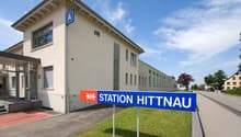 A building with a sign that reads 'Station Hittnau', a large window, and a red carpet leading to the entrance.