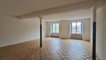 Empty room with wooden parquet flooring, white walls, two windows, and two pillars