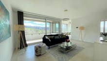 Spacious living room with large windows offering a scenic view, black sofa, glass coffee table, area rug, and decorative lamps