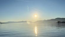 a lake with calm water, mountains in the background, two ducks, blue sky, sunset