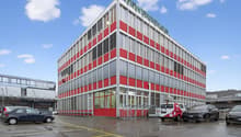 Large office building with red and gray exterior, multiple windows, several cars parked in front
