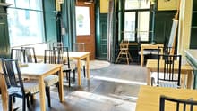 Wooden floor, rectangular dining tables, wooden chairs with striped cushions, green walls, wooden door, large windows, ceiling lamps
